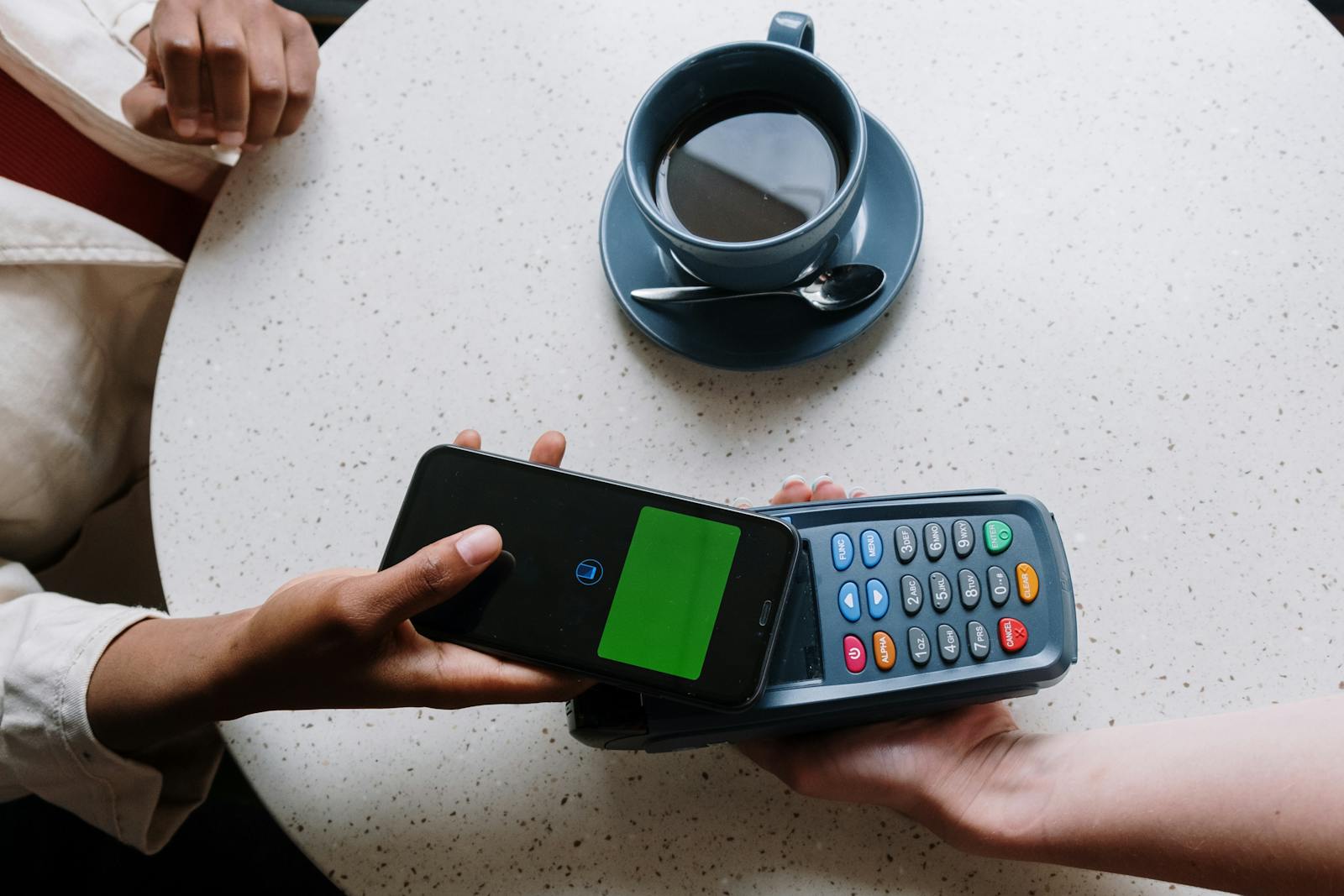 Contactless payment using a smartphone and card reader at a coffee shop table.
