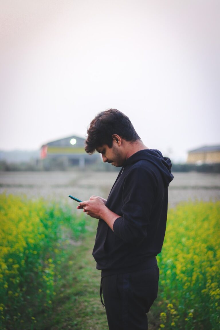 a man standing in a field looking at his cell phone