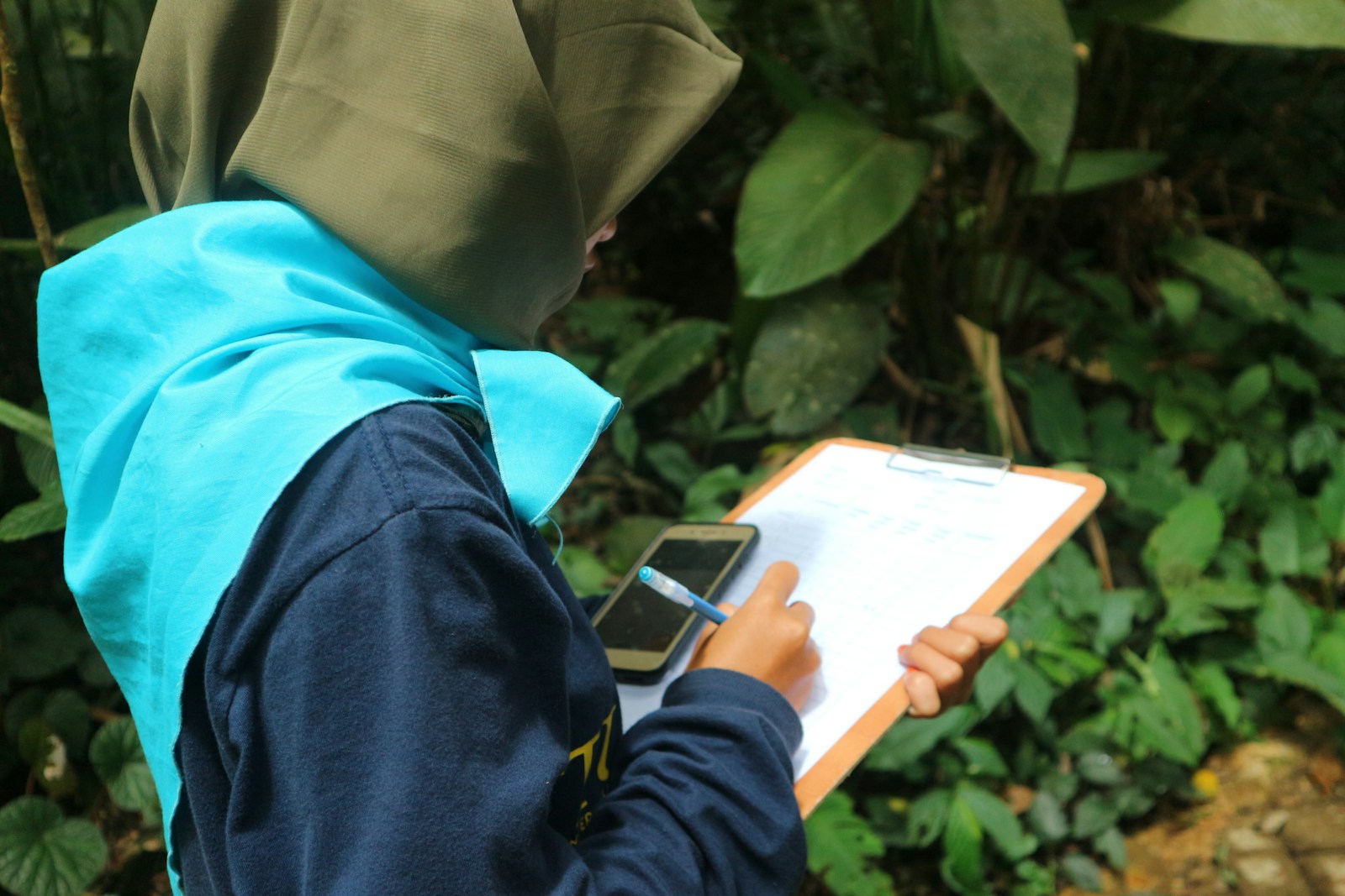 a person in a hijab writing on a clipboard
